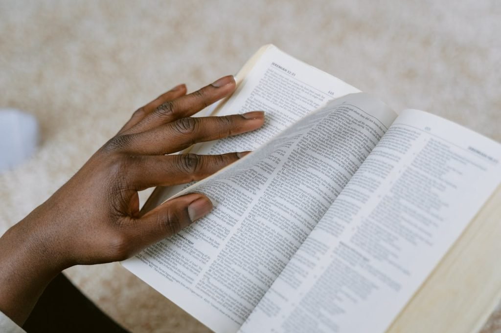 A person reads a page from the Holy Bible, focusing on scripture with a thoughtful hand turning the pages.